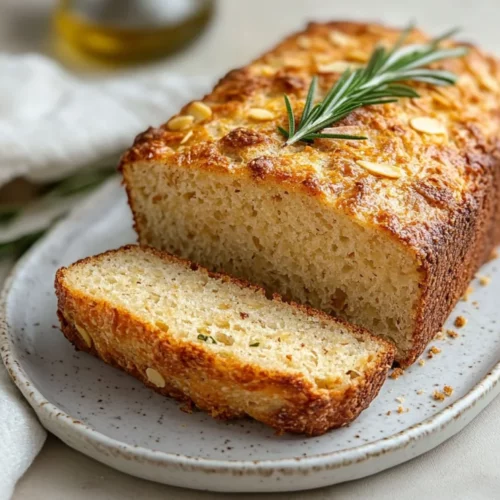 Freshly Sliced Almond Flour Bread Easy On A White Plate, Garnished With Rosemary, Showing Golden Crust And Soft Texture.