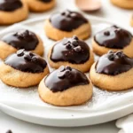 Classic Buckeye Cookies With Chocolate On A White Plate Lined With Parchment Paper, Garnished With Chocolate Chips And Powdered Sugar