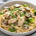 Creamy Chicken Pasta With Brussels Sprouts Served In A White Bowl, Garnished With Fresh Chives And Mushrooms.