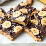 Frozen Peanut Butter Banana Bark Layered With Peanut Butter, Banana Slices, And Chocolate, Topped With Sea Salt On A Parchment-Lined Plate