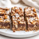 Gooey Gluten Free Magic Cookie Bars With Toasted Coconut, Chocolate Chips, And Nuts On A White Plate Lined With Parchment Paper