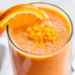 Vibrant Orange Healthy Carrot And Orange Smoothie In A Clear Glass, Garnished With Orange Slice And Zest, On A White Surface