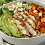 Healthy Chicken Quinoa Salad In A White Bowl Topped With Avocado, Feta, And Sunflower Seeds