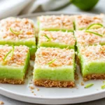 Low-Carb Coconut Lime Bars On A White Plate, Garnished With Toasted Coconut And Lime Zest Curls