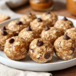 Close-Up Of No-Bake Energy Bites On A White Plate, Dotted With Chocolate Chips And Oats, With A Drizzle Of Honey.