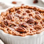 Slice Of Pecan Pie Dump Cake In A White Dish, Topped With Powdered Sugar And Fresh Pecans