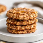 A Stack Of Vegan No-Bake Cookies On A White Plate Drizzled With Almond Butter And Sprinkled With Cinnamon, On A Clean Background