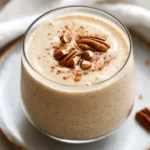 Delicious Apple Smoothie With Cider In A Clear Glass, Topped With Cinnamon And Pecans, On A White Plate