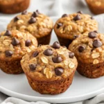 Freshly Baked Banana Oatmeal Muffins On A White Plate With Chocolate Chips, Topped With A Soft Kitchen Towel