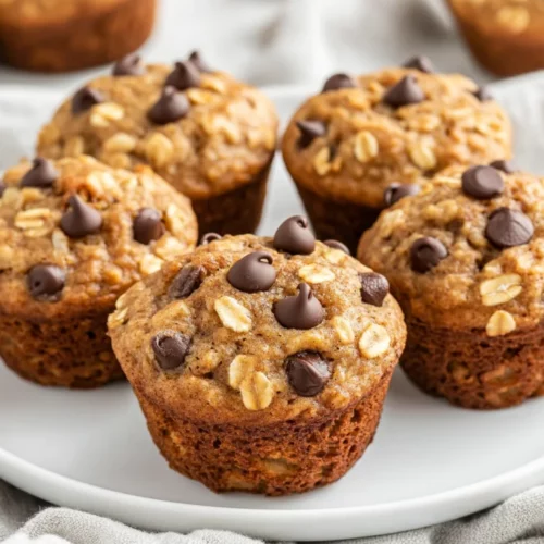 Banana Oatmeal Muffins: A Healthy &Amp; Easy Breakfast Treat 2 Freshly Baked Banana Oatmeal Muffins On A White Plate With Chocolate Chips, Topped With A Soft Kitchen Towel