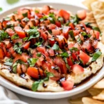 Bruschetta Dip Appetizer Garnished With Fresh Basil And Tomatoes On A White Platter With Pita Chips