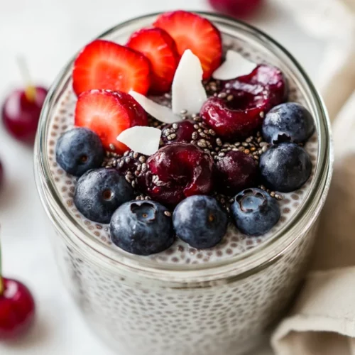 Chia Seed Pudding In A Clear Jar Topped With Blueberries And Cherries, Served With A Sprinkle Of Coconut Flakes.
