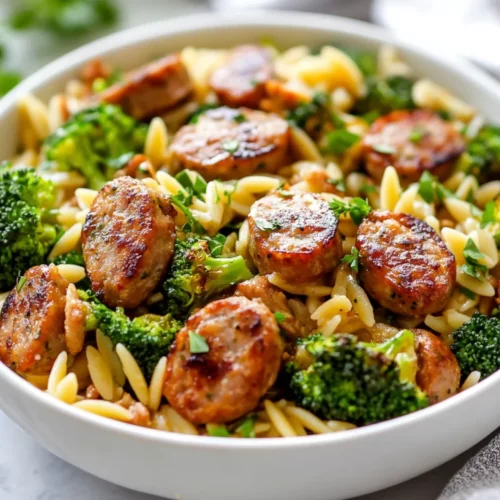 Colorful Chicken Sausage Orzo Broccoli In A Bowl, Garnished With Parsley And Pepper, On A Neutral Kitchen Countertop.
