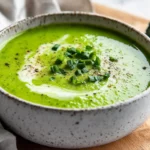 Bowl Of Cream Of Broccoli Soup Garnished With Chives And Broccoli Florets On A Wooden Cutting Board
