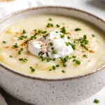 Bowl Of Creamy Potato Soup Topped With Sour Cream And Fresh Chives On A Wooden Table