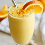 Creamy Turmeric Smoothie With Orange In A Tall Glass, Topped With Kefir And Garnished With Orange Zest