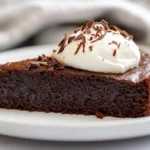 Flourless Chocolate Cake On A White Plate Topped With Whipped Cream And Chocolate Shavings