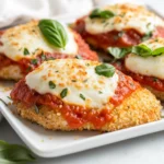 Crispy Gluten Free Chicken Parmesan On A White Plate Topped With Melted Cheese And Fresh Basil