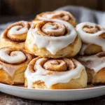 Stack Of Gluten-Free Cinnamon Rolls On A White Plate, Drizzled With Cream Cheese Frosting, Set On A Wooden Table
