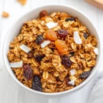 Close-Up Of Gluten Free Granola In A White Bowl, Garnished With Dried Fruit And Coconut Flakes