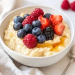 Bowl Of Gluten-Free Porridge Topped With Peanut Butter, Maple Syrup, And Fresh Berries On A White Plate