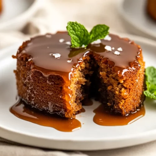 Gluten Free Sticky Toffee Pudding Served On A White Plate, Drizzled With Toffee Sauce And Garnished With Mint Leaves
