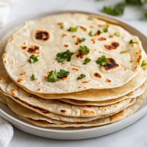Stack Of Soft Gluten-Free Tortillas On A White Plate, Garnished With Cilantro And Lime Wedges