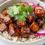 Bowl Of Gochujang Tempeh Bowls With Caramelized Tempeh, Brown Rice, And Pickled Vegetables Garnished With Cilantro.