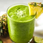 Green Pineapple Coconut Smoothie In A Clear Glass, Topped With Lime Zest And A Slice Of Lime, On A White Background