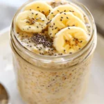 Bowl Of High-Protein Overnight Oats Topped With Banana Slices And Chia Seeds On A White Plate