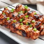 Grilled Korean Bbq Chicken Skewers On A White Plate Garnished With Green Onions And Sesame Seeds