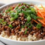 Korean Ground Beef Bowl With Brown Rice, Topped With Scallions And Carrots On A White Plate