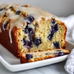 Slice Of Lemon Blueberry Banana Bread On A White Plate Showing Moist Texture And Lemon Glaze Drizzle