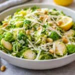 Parmesan Brussels Sprouts Salad In A White Bowl Garnished With Lemon Zest And Toasted Pine Nuts