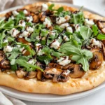 Roasted Mushroom Flatbread Pizza Topped With Goat Cheese And Arugula On A White Plate, Garnished With Cheese Shavings.