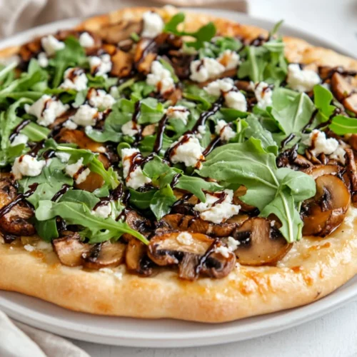 Roasted Mushroom Flatbread Pizza Topped With Goat Cheese And Arugula On A White Plate, Garnished With Cheese Shavings.
