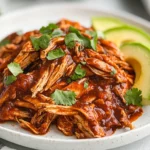 Slow Cooker Chipotle Chicken Served On A White Plate With Avocado Slices And Lime Wedges