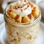 Bowl Of Apple Pie Overnight Oats Topped With Greek Yogurt And Cinnamon Apple Chunks, Served On A White Plate