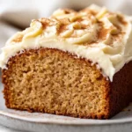 Slice Of Applesauce Cake With Cream Cheese Frosting On A White Plate, Garnished With Walnuts And Cinnamon