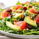 Vibrant Avocado Grapefruit Salad On A White Plate, Topped With Walnuts And Cranberries, Showcasing Bright Colors.