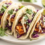 Appetizing Blackened Fish Tacos Topped With Crunchy Cabbage And Lime Wedges On A White Plate