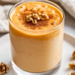 Creamy Carrot Cake Smoothie In A Clear Glass, Garnished With Crushed Walnuts And A Sprinkle Of Cinnamon