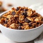 Bowl Of Chewy Grain-Free Banana Bread Granola Topped With Dark Chocolate Chips And A Sprinkle Of Cinnamon