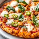 Crispy Chicken Crust Pizza Topped With Melted Cheese And Fresh Vegetables On A White Plate, Garnished With Basil