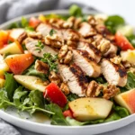 Colorful Chicken Waldorf Salad On A White Plate With Grilled Chicken, Apples, And Walnuts Garnished With Thyme.