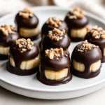Chocolate Peanut Butter Banana Bites On A White Plate Garnished With Crushed Nuts And A Drizzle Of Chocolate.