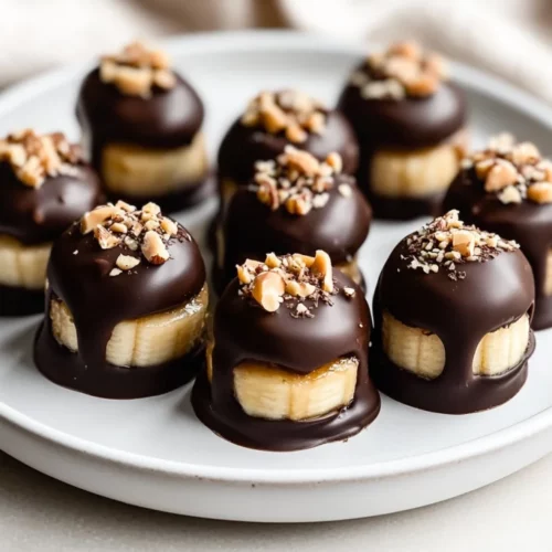 Chocolate Peanut Butter Banana Bites: A Healthy Frozen Treat 2 Chocolate Peanut Butter Banana Bites On A White Plate Garnished With Crushed Nuts And A Drizzle Of Chocolate.