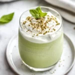 Creamy Coconut Matcha Shake Topped With Coconut Cream And A Mint Leaf Served On A White Plate