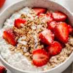 Cottage Cheese Breakfast Bowl Topped With Roasted Strawberries And Coconut Flakes, Drizzled With Maple Syrup