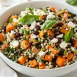 Couscous Salad With Lime Dressing In A White Bowl, Topped With Feta, Sweet Potatoes, Spinach, And Pistachios